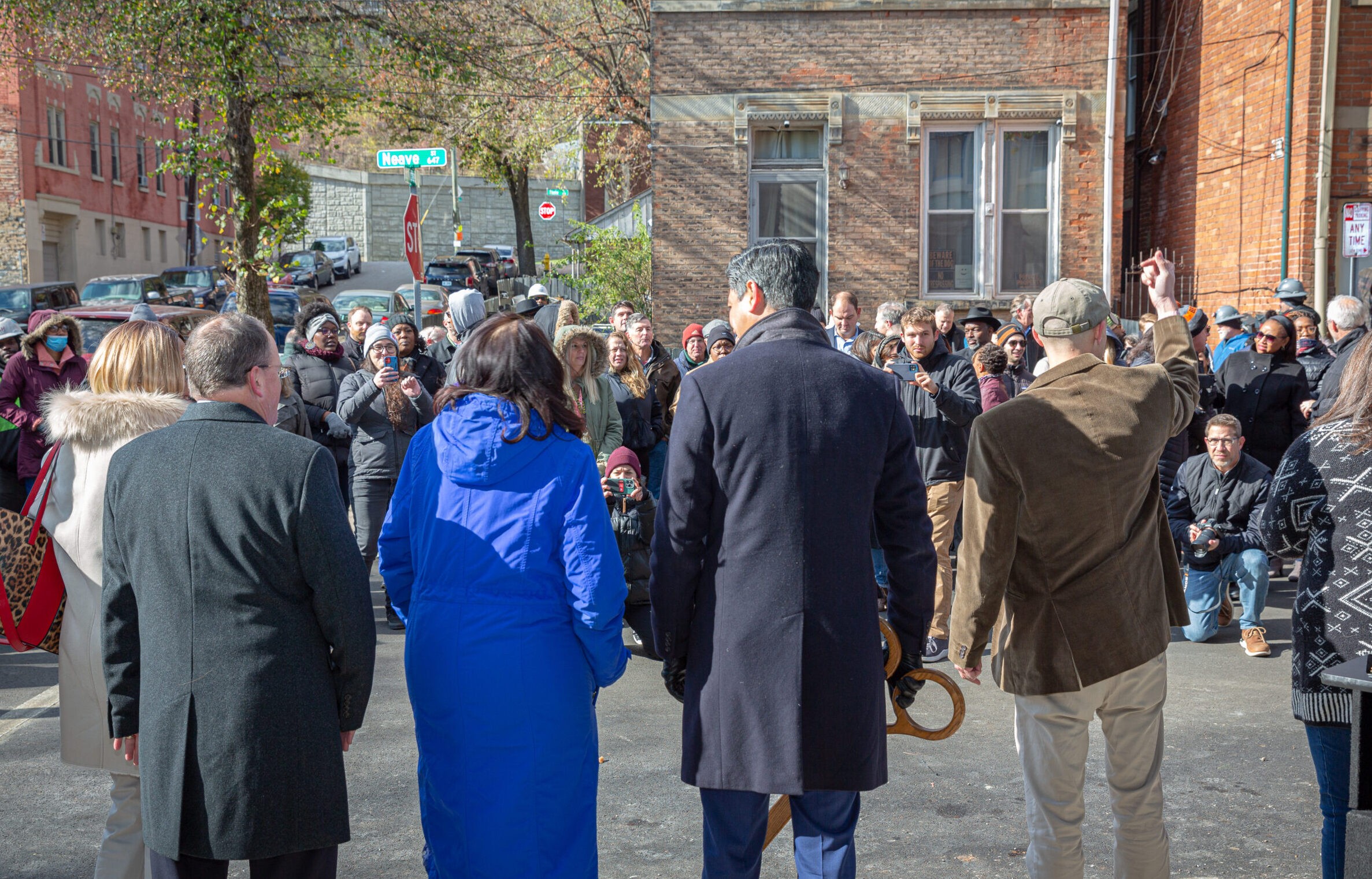 A small group of people look out at a crowd standing on a city street surrounding by brock buildings.