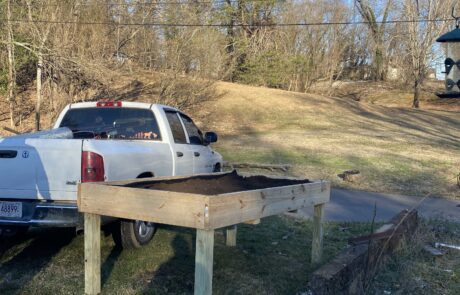 A photo of a completed accessible raised garden bed full of soil with a white truck next to it.